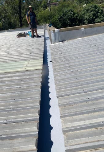 Scott & Sons plumber beside a box gutter between metal roof sections